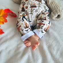 Load image into Gallery viewer, Baby wearing Halloween Dungarees, with Skeletons at a party. Burnt Oranges, Browns and Earthy Greens. Cute Baby Toes