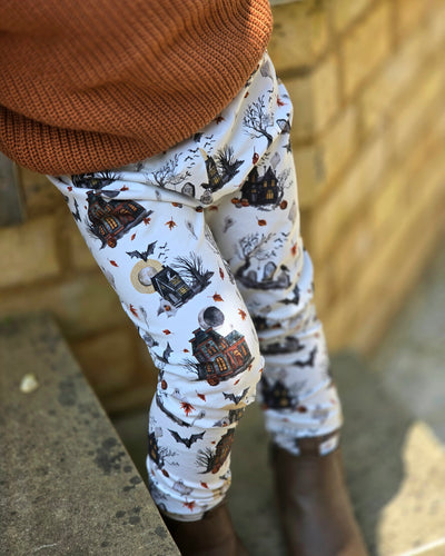 Off White Leggings with different Haunted Mansions. Bats, Ghost and Autumn Leaves surround them. Unisex Leggings