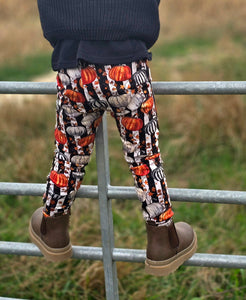 Child wearing Black & White Striped patterned leggings with pumpkins and brown boots standing on a metal gate. Toddler Halloween Clothes